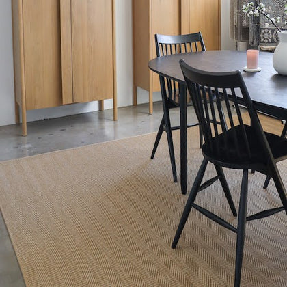 Arlen Dune area rug under a dining room table. Black chairs, a candle and flowers on the table
